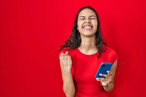 Junge Brasilianerin Mit Smartphone Über Rotem Hintergrund Sehr Glücklich Und — Stockfoto