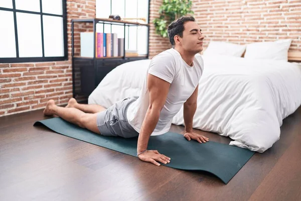 Young hispanic man stretching back sitting on floor at bedroom