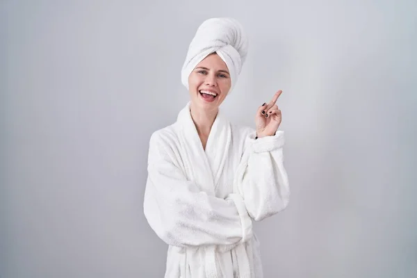 金发女人穿着浴衣 脸上挂着大大的笑容 手指头指向旁边看相机 — 图库照片