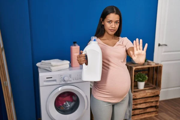妊娠中の若いです洗濯機を保持します洗剤ボトルで手を開きます真剣で自信を持って式で停止標識を行います 防衛ジェスチャー — ストック写真