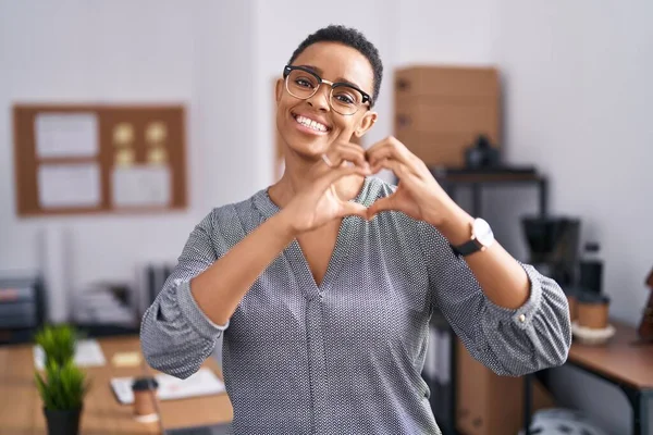 stock image African american woman working at the office wearing glasses smiling in love doing heart symbol shape with hands. romantic concept. 