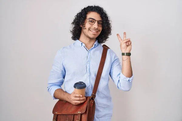 巻き毛を持つヒスパニック系の男は 勝利のサインを行う指を示すカメラを見て笑みを浮かべてコーヒーを飲む — ストック写真