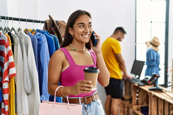 Young latin customer woman smiling happy talking on the smartphone at clothing store.