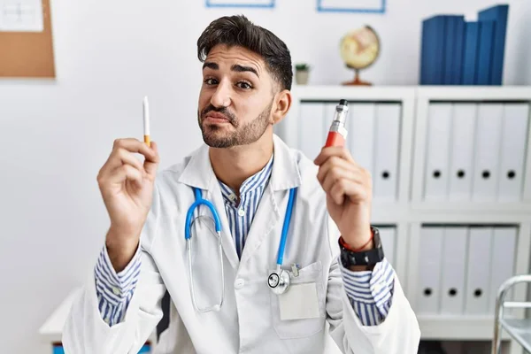 Joven Doctor Sosteniendo Cigarrillo Electrónico Clínica Médica Sonriendo Mirando Hacia —  Fotos de Stock