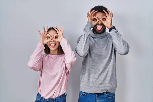 Young Hispanic Couple Standing Together Doing Gesture Binoculars Sticking Tongue — Stok fotoğraf