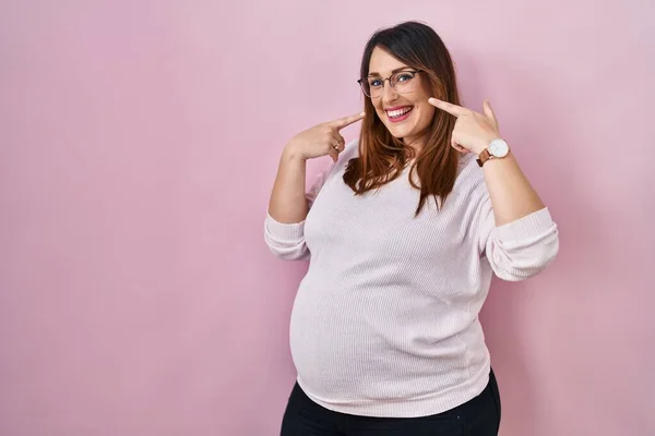 Těhotná Žena Stojí Nad Růžovým Pozadím Vesele Usmívá Ukazuje Ukazuje — Stock fotografie