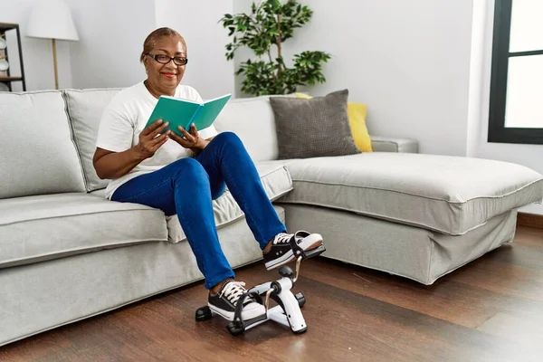 高级非洲裔美国妇女在家里用自行车踏板机看书做运动 — 图库照片