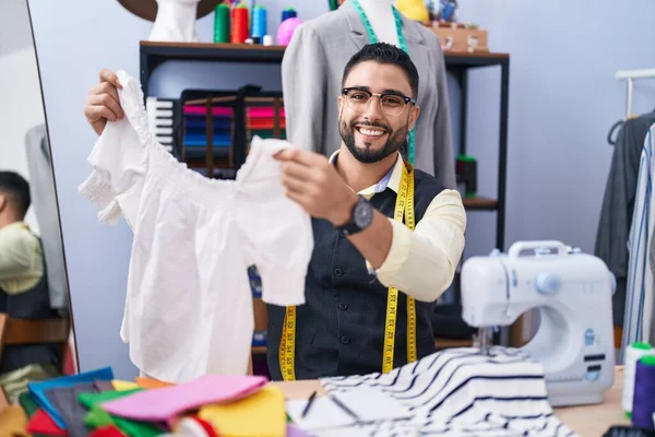 年轻的阿拉伯男子裁缝笑着自信地在服装厂拿着T恤 — 图库照片