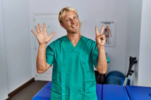 Young Blond Man Wearing Physiotherapist Uniform Standing Clinic Showing Pointing — Stockfoto