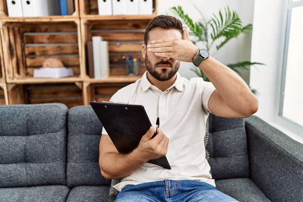 Handsome Hispanic Man Holding Clipboard Working Psychology Clinic Covering Eyes — Stock Photo, Image