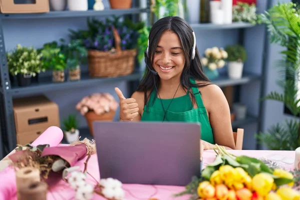 Brunette woman working at florist shop doing video call smiling happy and positive, thumb up doing excellent and approval sign