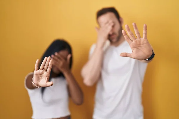 Interracial Couple Standing Yellow Background Covering Eyes Hands Doing Stop — Zdjęcie stockowe