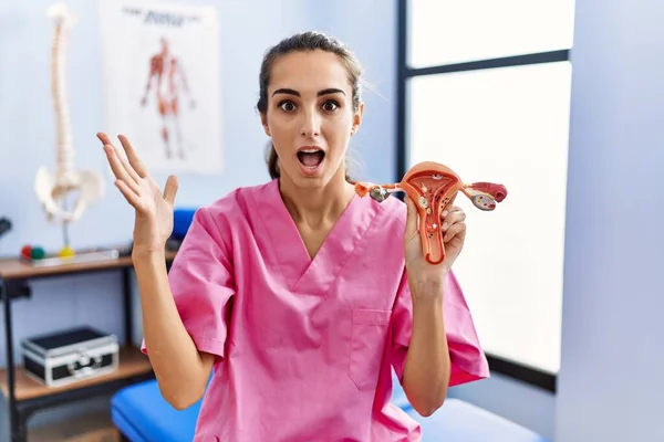 Young hispanic woman holding model of female genital organ at rehabilitation clinic celebrating victory with happy smile and winner expression with raised hands