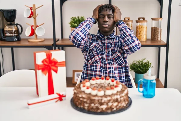 非洲男人拿着巨大的巧克力蛋糕庆祝生日 由于疼痛和偏头痛 绝望和压力重重 手放在头上 — 图库照片