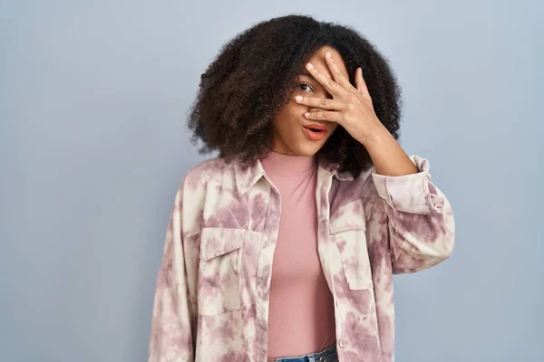 Young African American Woman Standing Blue Background Peeking Shock Covering — Stockfoto