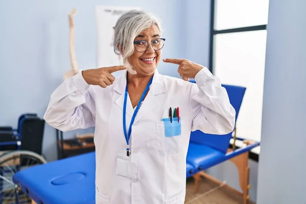 痛み回復クリニックで働く白髪の中年女性は 明るい表情と指の歯と口で指して笑っています 歯の健康の概念 — ストック写真