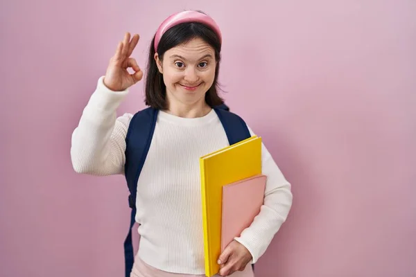 ダウン症候群の学生のバックパックを着て 手や指でOkサインをやって肯定的な笑顔本を保持する女性 成功した表現 — ストック写真