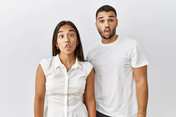 Young interracial couple standing together in love over isolated background making fish face with lips, crazy and comical gesture. funny expression.