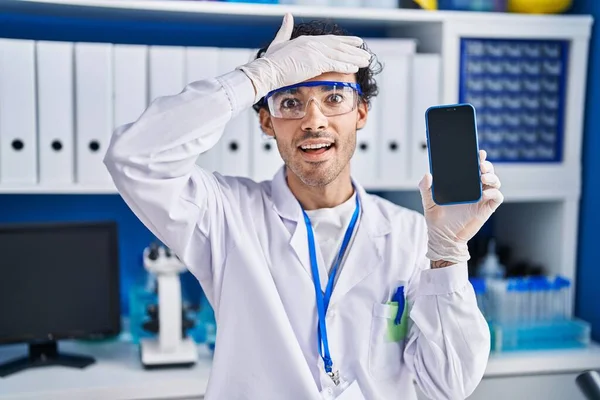スマートフォンの画面を示す科学研究所で働いているヒスパニック系の男は強調し 頭の上に手で不満 驚きと怒っている顔 — ストック写真