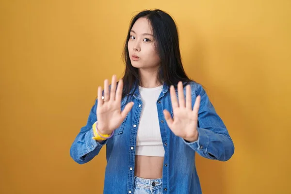 黄色の背景の上に立つ若いアジアの女性は 恐怖と嫌な表情で拒否と否定を示す手のひらを離れて移動します 止めて禁止する — ストック写真