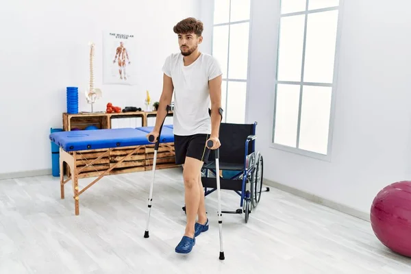Young arab man patient walking using crutches at clinic