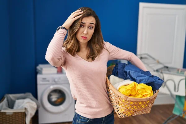 Young woman holding laundry basket worried and stressed about a problem with hand on forehead, nervous and anxious for crisis
