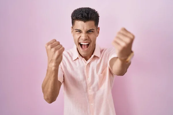 Mladý Hispánec Stojící Nad Růžovým Pozadím Zuřivě Vztekle Pozvedal Pěsti — Stock fotografie