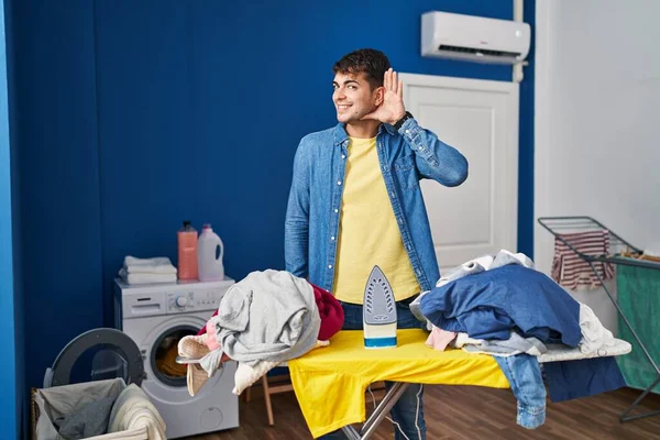 Young Hispanic Man Ironing Clothes Home Smiling Hand Ear Listening — Stock Photo, Image