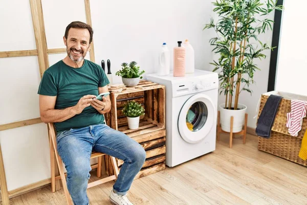 Middle Age Hispanic Man Doing Laundry Using Smartphone Waiting Home — Fotografia de Stock