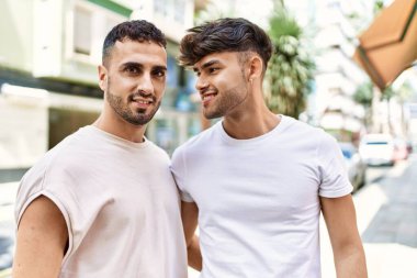 İki İspanyol erkek gülümsüyor. Kendilerine güveniyorlar. Sokakta birbirlerine sarılıyorlar.