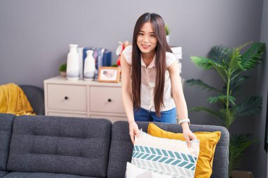 Young chinese woman smiling confident organize sofa at home