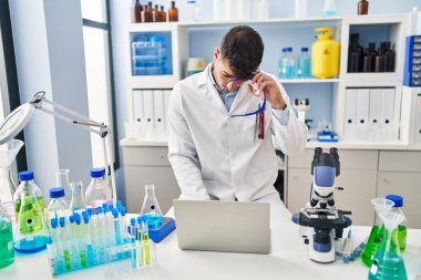 Young hispanic man scientist stressed using laptop working at laboratory