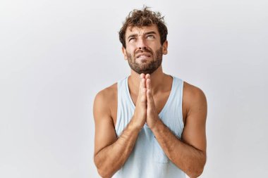 Soyutlanmış arka planda duran yakışıklı genç adam elleri bağlı yalvarıyor ve dua ediyor. Yüzünde umut ifadesi var. Çok duygusal ve endişeli. Yalvarıyor. 