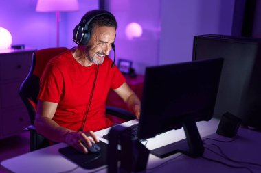 Middle age man streamer playing video game using computer at gaming room
