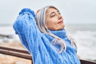 Orta yaşlı, kır saçlı, gülümseyen, kendine güvenen bir kadın.