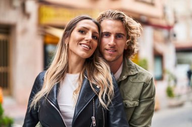 Kadın ve erkek gülümsüyor. Kendilerine güveniyorlar. Sokakta sarılıyorlar.