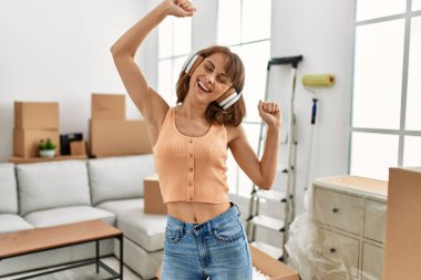 Genç beyaz kadın, kendinden emin bir şekilde gülümsüyor. Evde müzik dinliyor ve dans ediyor.