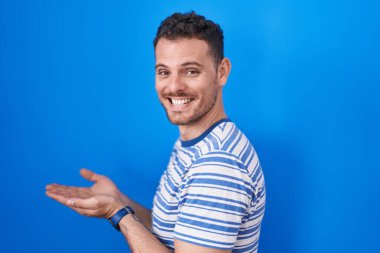 Mavi arka planda dikilen genç İspanyol adam avuçlarını açıp fotokopi alanını gösteriyor. 