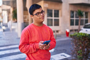 Down syndrome man smiling confident using smartphone at street