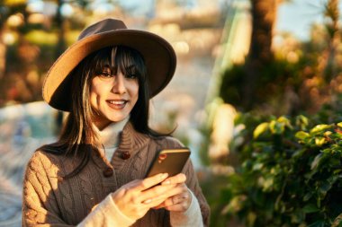 Parkta akıllı telefon kullanarak gülümseyen esmer kadın.