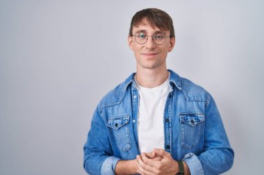 Caucasian blond man standing wearing glasses with hands together and crossed fingers smiling relaxed and cheerful. success and optimistic 