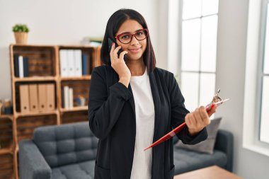 Klinikteki akıllı telefondan konuşan genç Latin kadın psikolog.