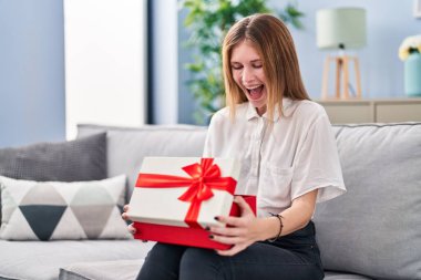 Güzel bir kadın hediyesini tutarak çılgınlığı kutluyor ve başarıya hayret ediyor gözleri açık heyecanla haykırıyor. 