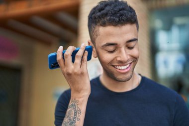 Afro-Amerikalı adam gülümsüyor. Caddedeki akıllı telefondan kendine güvenen bir sesli mesaj dinliyor.