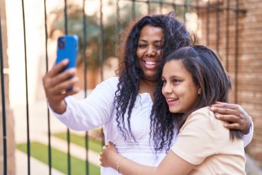 Mother and daughter hugging each other make selfie by smartphone at street