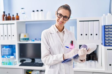 Young woman scientist writing on clipboard at laboratory