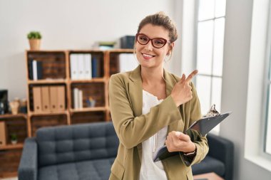 Muayenehanede çalışan genç bir kadın, elini kenarı işaret ederek ciddi ve sakin bir yüz ifadesi sergiliyor. 