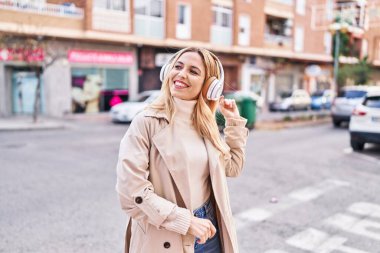 Young blonde woman listening to music and dancing at street