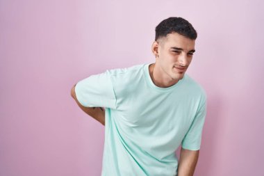 Yakışıklı İspanyol adam pembe arka planda duruyor sırt ağrısı çekiyor, elleriyle dokunuyor, kas ağrısı çekiyor. 