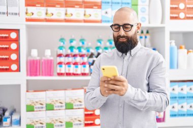 Young bald man customer smiling confident using smartphone at pharmacy
